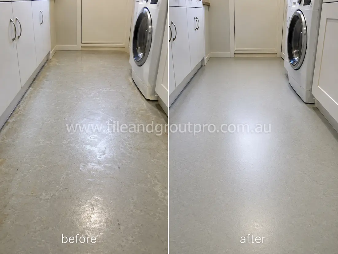 Laundry room with grey linoleum floors before sealer stripping, featuring dull patches, moisture staining, worn protective coating, and surface scuffs around cabinets and washing machine.