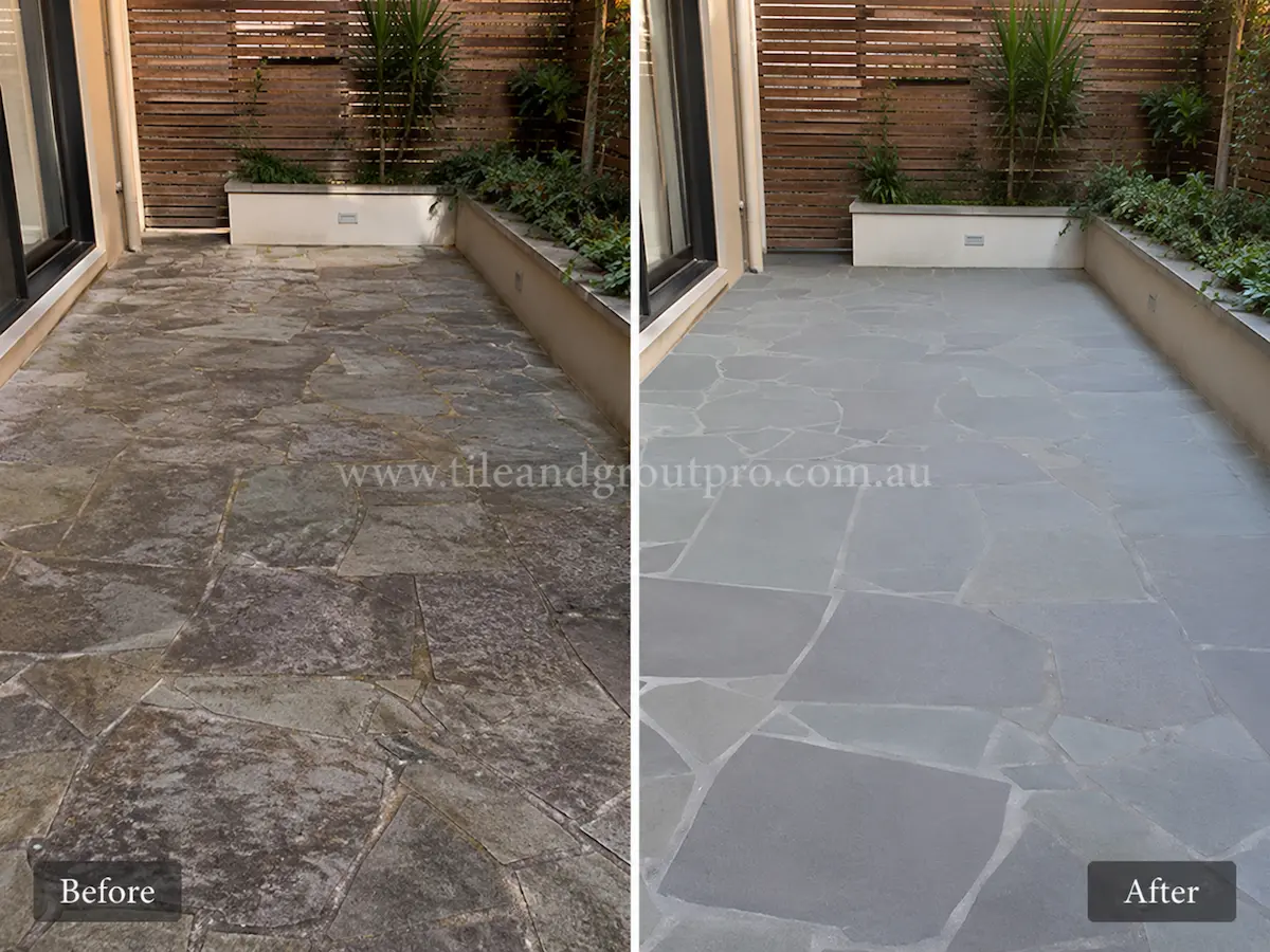 Bluestone crazy paving courtyard before sealer stripping showing uneven sealer haze and weathered natural stone pieces in a narrow landscaped outdoor space.