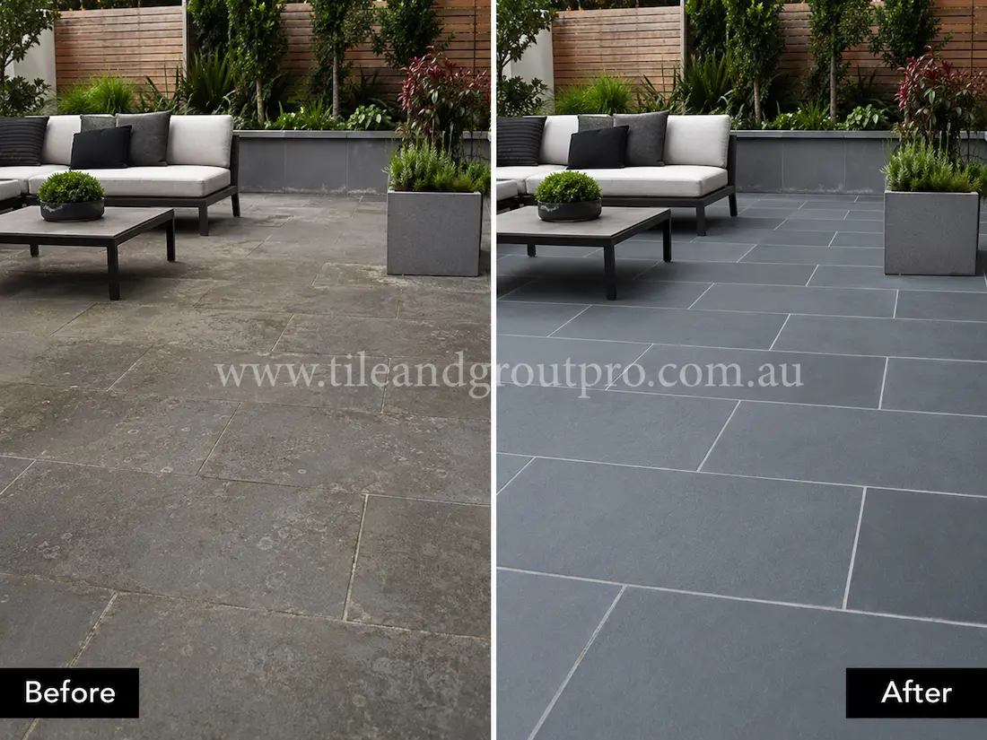 Before tile renewal, outdoor bluestone patio tiles in a modern courtyard lounge area appeared faded and patchy with visible residue, weathering, and uneven stone colouring around the outdoor furniture.
