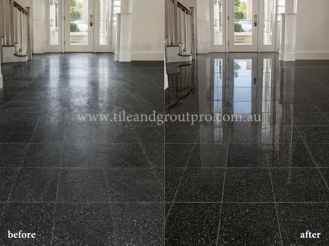 Before stone polishing, the black granite foyer floor tiles had a cloudy, dull finish with visible traffic wear in a bright residential entrance with staircase and glass front doors.