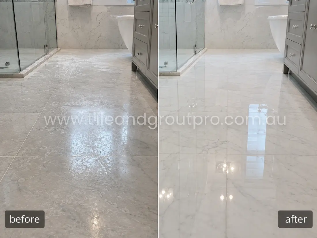 Modern bathroom marble floor tiles before grinding, showing etched patches, dull stone finish, light scratches, and water staining near the shower and vanity area.