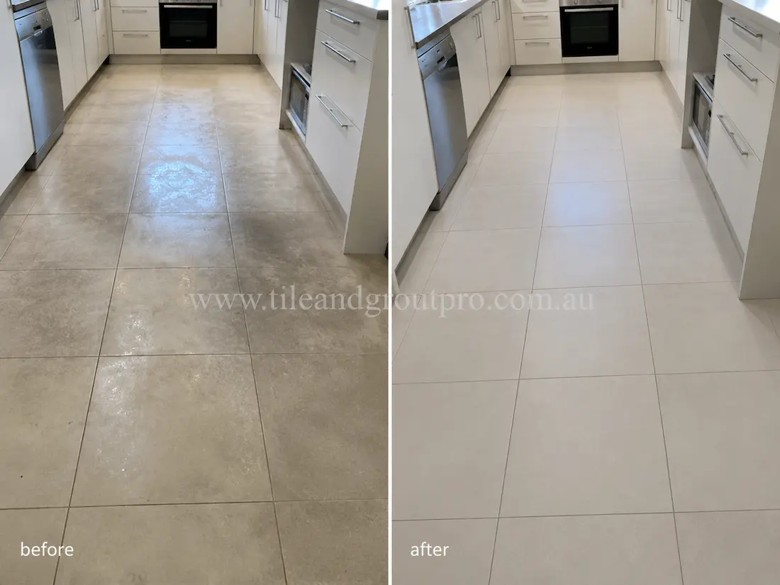 Modern kitchen with large light-grey porcelain floor tiles before sealer stripping, displaying visible sealer haze, patchy gloss, and worn residue across the cooking area.