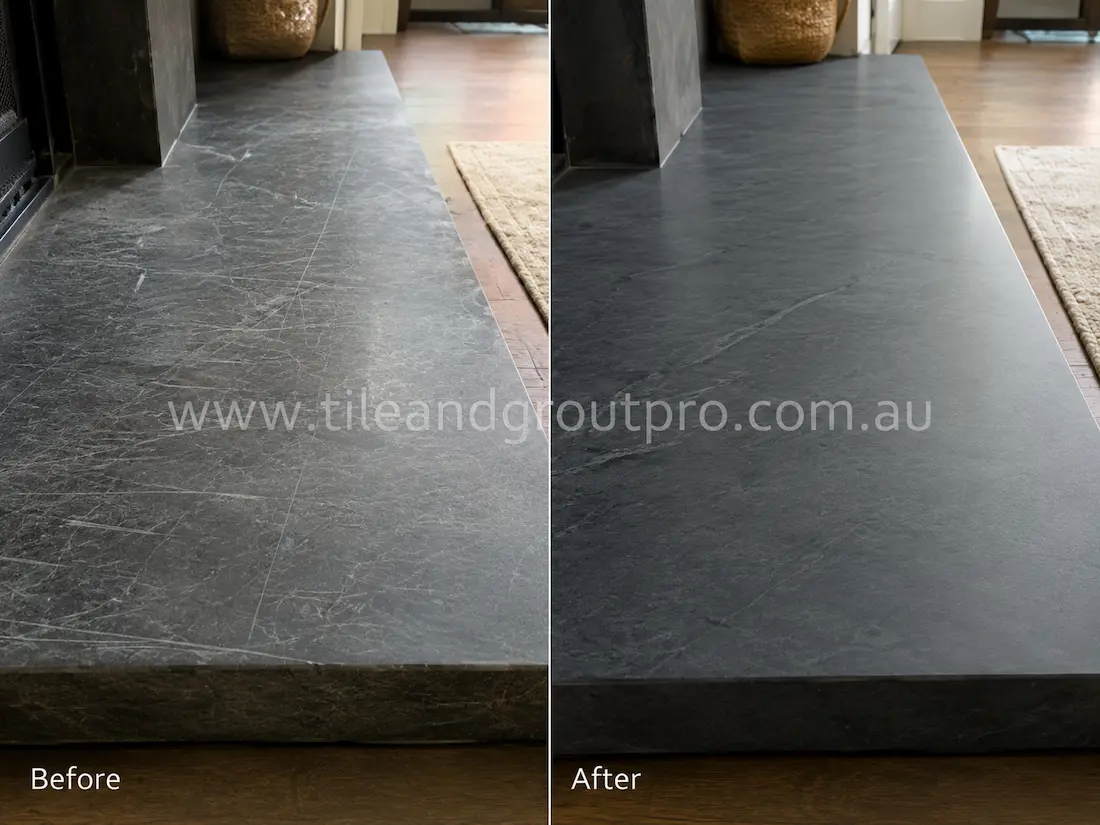 Scratched dark soapstone fireplace hearth before scratch removal in a contemporary living room interior.
