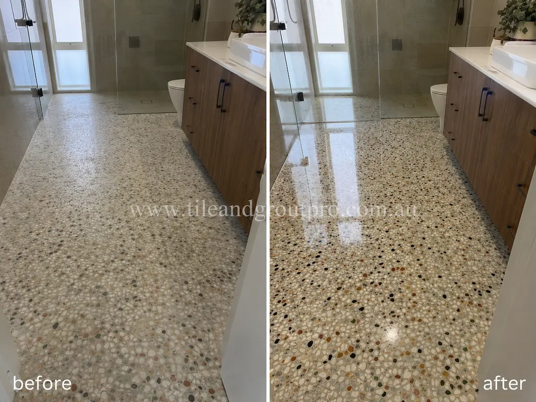 Before stone polishing, the terrazzo bathroom floor appeared flat and low-sheen with subdued aggregate texture near a timber vanity, glass shower screen, and frosted window.