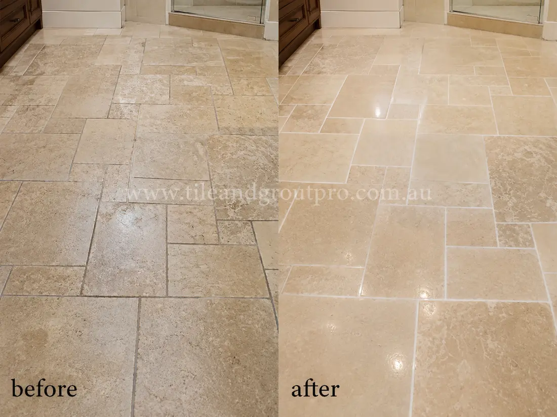 Bathroom travertine tile floor before grinding, featuring etched stone surfaces, dull patches, and worn grout lines beside the vanity and shower area.