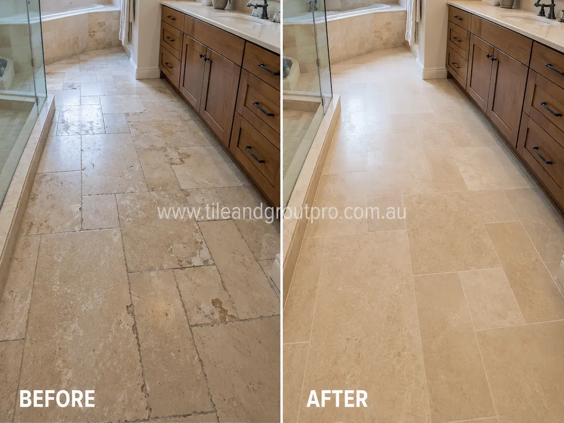 Master bathroom with travertine floor tiles around a vanity and shower area, showing worn stone surfaces, staining, and faded appearance before tile resurfacing.